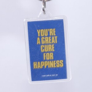 Peut inclure: Un porte-clés bleu avec une inscription jaune qui dit "You're a great cure for happiness".