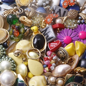 Op de afbeelding: Een grote verzameling kleurrijke en unieke oorbellen. De oorbellen zijn gemaakt van verschillende materialen, waaronder metaal, plastic en glas. Sommige oorbellen zijn versierd met kralen, stenen en andere versieringen. De oorbellen zijn willekeurig gerangschikt op een wit oppervlak.