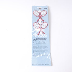 May include: A package of Wrights Appliques featuring two pairs of red and white tennis rackets. The package is blue and white with the text "Wrights Appliques are the "Right Touch" to dress up a shirt, jacket or other apparel."