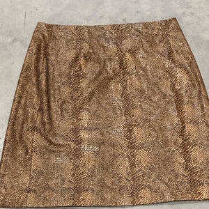 May include: A brown and tan snakeskin-patterned skirt. The skirt is a-line and appears to be made of a faux leather material. The skirt is a neutral color and could be paired with many different tops.
