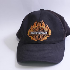 May include: Black baseball cap with an embroidered Harley-Davidson logo featuring flames in orange and yellow.