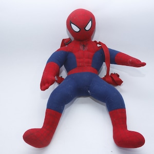 May include: Red and blue plush Spider-Man backpack toy. The toy has a red and blue suit with a spider logo on the chest. The toy has a strap on each shoulder.