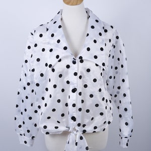 May include: White sheer blouse with black polka dots and a tie front. The blouse has long sleeves and a v-neck.