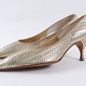 May include: A pair of gold high-heeled shoes with a pointed toe and a perforated design.