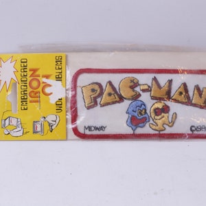Op de afbeelding: Strijk-op patch met Pac-Man, een geel personage met een mond, en twee geesten. De patch is wit met rode en gouden borduurwerk. De tekst "PAC-MAN" is in goud en de tekst "MIDWAY" is in zwart. De tekst "1981" is in zwart.