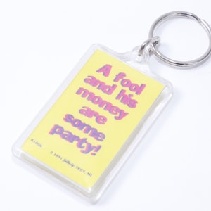 May include: A yellow keychain with a clear plastic frame and a silver key ring. The keychain has the text "A fool and his money are some party!" printed on it.