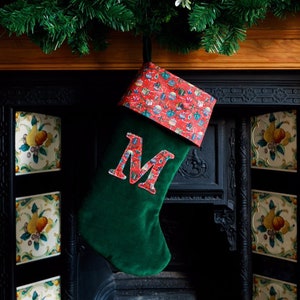 Peut inclure: Une chaussette de Noël en velours vert avec un revers à motif rouge et blanc. La chaussette a une grande lettre "M" brodée sur le devant.