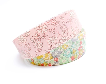 May include: Two fabric headbands with floral patterns. The top headband is pink with a white floral design. The bottom headband is green with a multi-colored floral design.