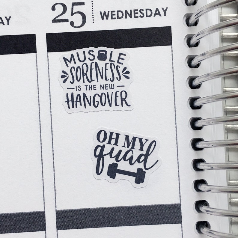 Op de afbeelding: Twee witte stickers met zwarte tekst en een haltergrafiek. De eerste sticker zegt "Muscle Soreness - Is the new - Hangover". De tweede sticker zegt "Oh My Quad" met een haltergrafiek.