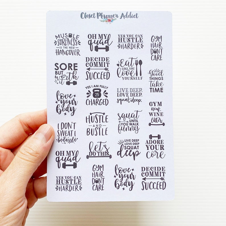 Op de afbeelding: Een vel met witte stickers met zwarte motiverende citaten en zinnen over fitness en lichaamsbeweging. De citaten omvatten "Oh my quad", "Hustle harder", "Love your body", "Decide commit succeed" en "Live deep love deep squat deep".