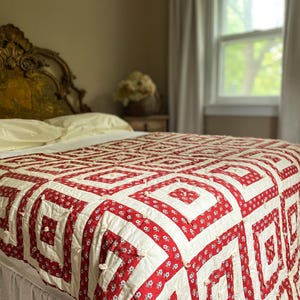 May include: A rectangular quilt featuring a repeating square pattern in red and white. The red fabric displays a small floral print, while the white fabric is solid. The quilt is tied with small white knots at the center of each square block.