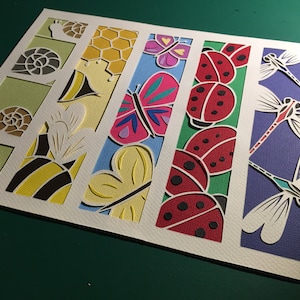 Puede incluir: Una obra de arte recortada en papel con varios insectos y elementos de la naturaleza. El diseño incluye caracoles, abejas, un panal, mariposas, mariquitas y libélulas, cada uno en un color diferente y sobre un fondo de color.