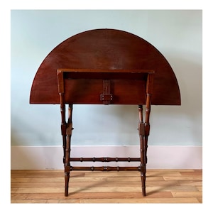 May include: A dark brown wooden folding table with a half-circle top and a shelf underneath. The table has a bamboo-style base with four legs.