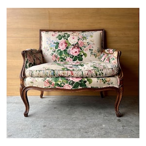 May include: A vintage floral patterned armchair with a wooden frame and carved legs. The chair has a floral patterned fabric upholstery with pink and green roses.