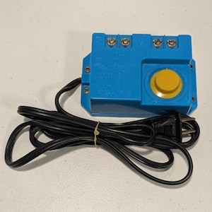 May include: A blue rectangular electronic controller featuring a prominent yellow circular dial on the right side, four metal screw terminals along the top edge, and a long black power cord with a standard two-prong electrical plug attached.