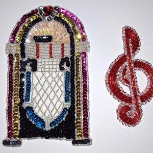 May include: Two decorative patches: a jukebox and a treble clef. The jukebox patch is adorned with sequins in various colors, including black, gold, pink, and blue. The treble clef is red with silver accents, both patches are on a white background.