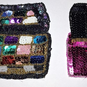 May include: Two beaded cosmetic items. One is a black and multi-colored sequined makeup palette. The other is a pink and black sequined nail polish bottle. Both items are embellished with black and gold beads.