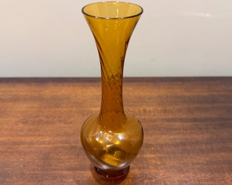 Puede incluir: Jarrón de cristal color ámbar con diseño en espiral en el tallo. El jarrón tiene una base redondeada y una parte superior acampanada. El cristal tiene un acabado brillante, que refleja la luz. El jarrón mide unos 23 cm de alto.