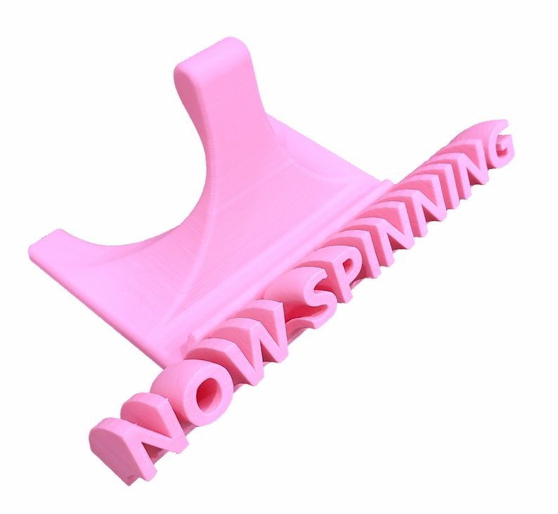 K&ouml;nnte beinhalten: Ein rosa 3D-gedruckter Telefonst&auml;nder mit den Worten "NOW SPINNING" auf der Seite.
