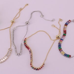 May include: Four adjustable bracelets with different colored stones. Two bracelets have clear stones, one has rainbow colored stones, and one has a mix of pink, purple, and green stones.