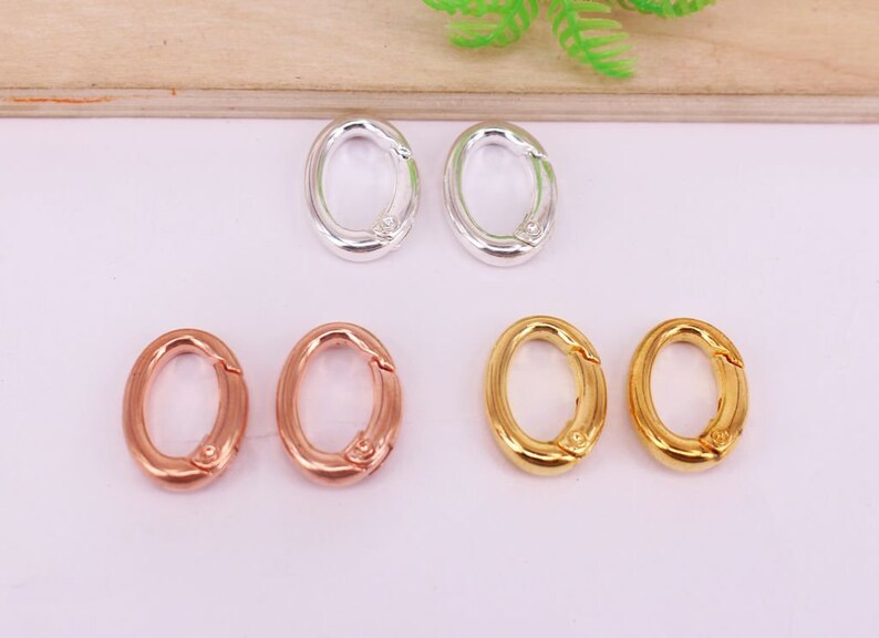 May include: An assortment of oval-shaped clasps in silver, rose gold, and gold tones. The clasps are shown open and closed, showcasing their functionality. These jewelry findings are ideal for various crafting projects.