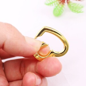 May include: A gold-colored heart-shaped metal clasp with a spring-loaded opening.