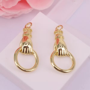 May include: Two gold-toned metal hand-shaped charms with a ring attached to each hand. The charms are designed to look like a hand holding a ring.
