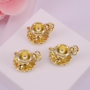 May include: Three gold-tone teacup charms with a saucer and spoon. Each charm has a loop for attaching to a necklace or bracelet.