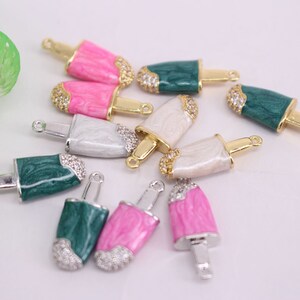 Puede incluir: Surtido de abalorios de paleta de colores con detalles dorados y plateados. Los abalorios est&aacute;n hechos de esmalte y presentan una variedad de colores, incluyendo rosa, verde y blanco. Cada abalorio tiene un bucle en la parte superior para sujetarlo a un collar, pulsera u otras joyas.