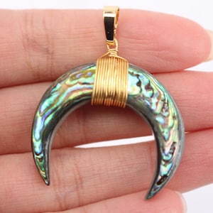 May include: A gold-wrapped abalone shell crescent moon pendant. The pendant has a iridescent green, blue, and purple color.
