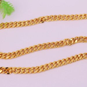 Op de afbeelding: Een gouden ketting met een curb-link stijl. De ketting ligt plat op een roze oppervlak.