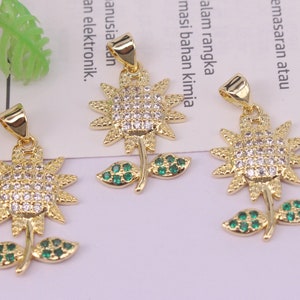 Op de afbeelding: Drie gouden zonnebloembedels met heldere en groene strasssteentjes. Elke bedel heeft een lus om aan een ketting of armband te bevestigen.