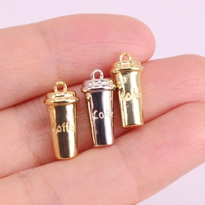 May include: Three gold and silver charm pendants shaped like coffee cups. Each cup has the word "Coffee" printed on it.