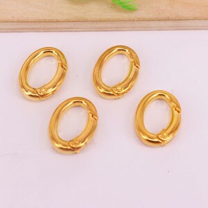 May include: Four gold-colored oval-shaped clasps. Each clasp has a hinged opening mechanism. The clasps are arranged on a light background, suggesting they are jewelry findings or components for accessories.