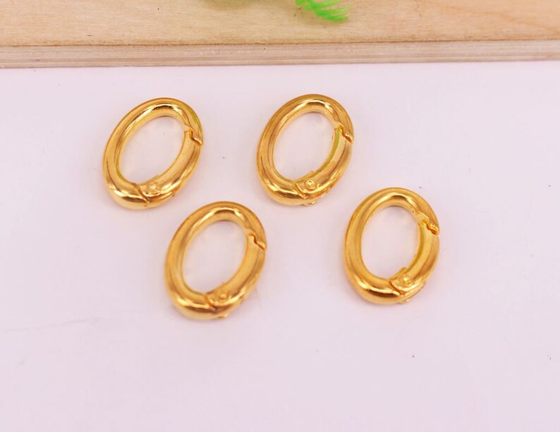 May include: Four gold-colored oval-shaped clasps. Each clasp has a hinged opening mechanism. The clasps are arranged on a light background, suggesting they are jewelry findings or components for accessories.