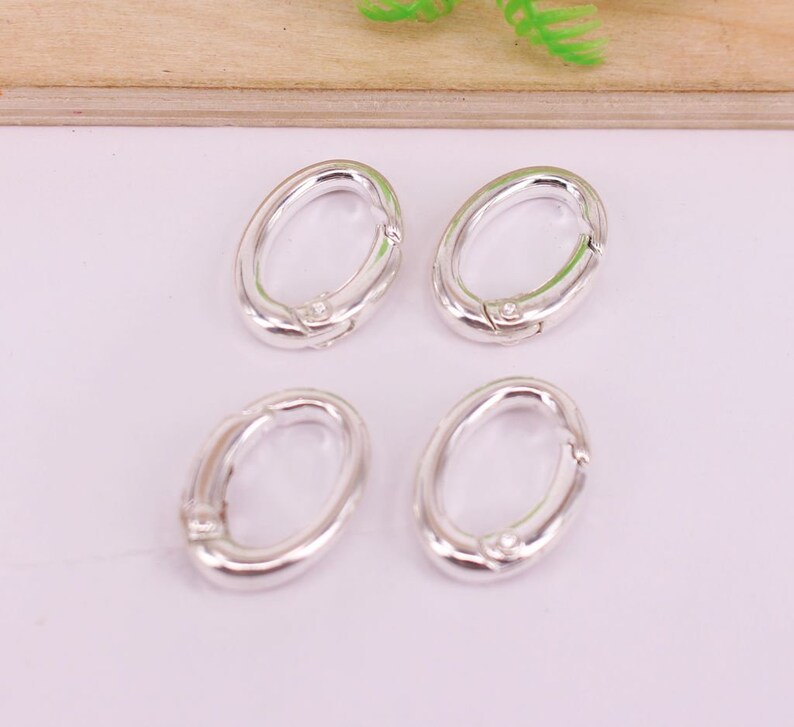 May include: Four silver-colored oval-shaped clasps arranged in a square. Each clasp has a hinged mechanism for opening and closing. The clasps are made of a shiny, metallic material.