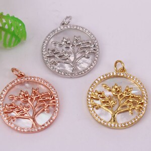 May include: Three round pendants featuring a tree of life design. The pendants are crafted from metal and have a white mother of pearl inlay. The pendants are encircled by a circle of clear rhinestones. The pendants are available in silver, gold, and rose gold.