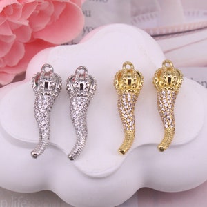 May include: Four ornate, gold and silver, horn-shaped charms with a crown design and clear crystal embellishments. The charms are displayed on a white surface.