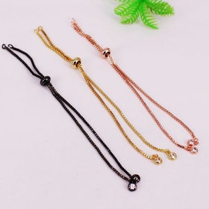 May include: Three adjustable bracelet cords with a sliding bead and clear crystal accents. The cords are black, gold, and rose gold.