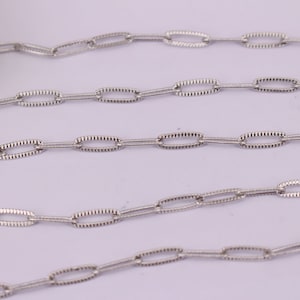 May include: A silver chain with oval links. The links have a textured surface.