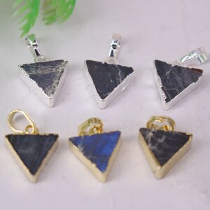 Puede incluir: Seis colgantes en forma de triángulo hechos de piedra labradorita con detalles en oro y plata. Los colgantes miden aproximadamente 2 cm.