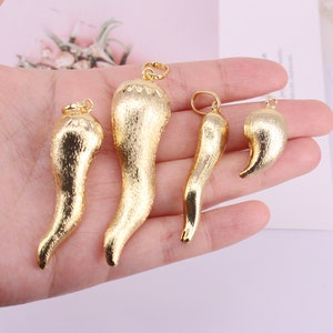 May include: Four gold-colored, textured chili pepper charms with small loops for jewelry making. The charms vary in size, with the largest being approximately 2 inches long. The charms are held in a hand.