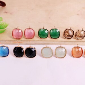 May include: Eight pairs of square-shaped earrings with gold settings. The earrings feature faceted glass stones in a variety of colors, including pink, green, brown, blue, black, white, and orange.
