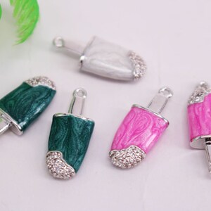Puede incluir: Cinco colgantes de plata con forma de polos con diferentes colores de esmalte y detalles de pedrer&iacute;a. Los colores son blanco, verde, rosa y un verde m&aacute;s oscuro.