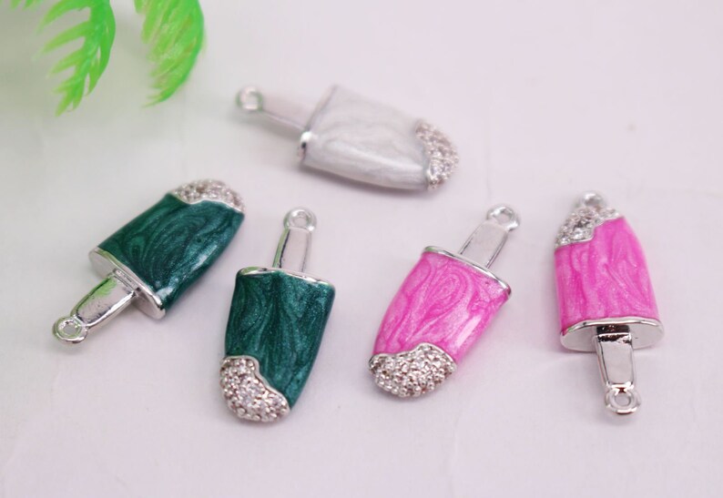 Puede incluir: Cinco colgantes de plata con forma de polos con diferentes colores de esmalte y detalles de pedrer&iacute;a. Los colores son blanco, verde, rosa y un verde m&aacute;s oscuro.