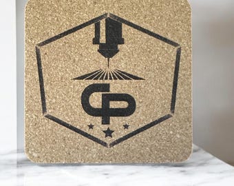 May include: Square cork coaster with a laser-etched design. The design features a hexagon with a laser machine graphic, the letters "CP", and three stars. The coaster is light brown and sits on a white marble surface.
