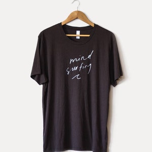 May include: A dark brown t-shirt with the text "mind surfing" written in white on the front.