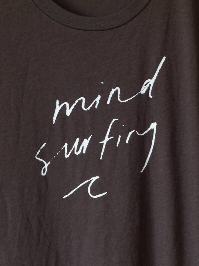 May include: A dark brown t-shirt with the words "mind surfing" written in white cursive script. A small wave graphic is below the text.