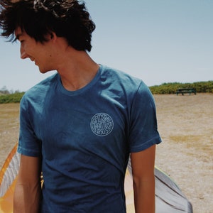 May include: A blue t-shirt with the text "SOME THOUGHTS EXIST" in a circular design. The shirt is worn by a person outdoors on a sunny day. The shirt has short sleeves and a crew neck.