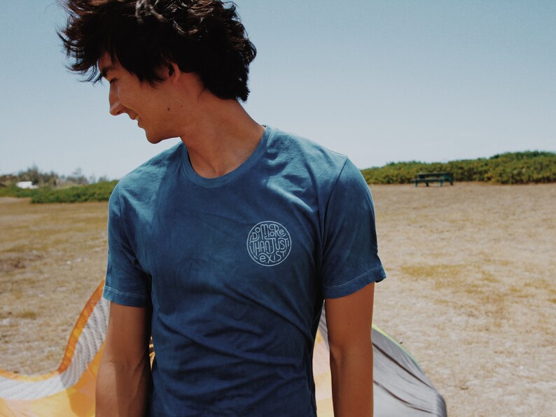 May include: A blue t-shirt with the text "SOME THOUGHTS EXIST" in a circular design. The shirt is worn by a person outdoors on a sunny day. The shirt has short sleeves and a crew neck.